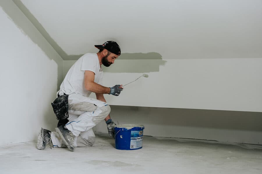Maler arbeitet knieend an der unteren Wandfläche