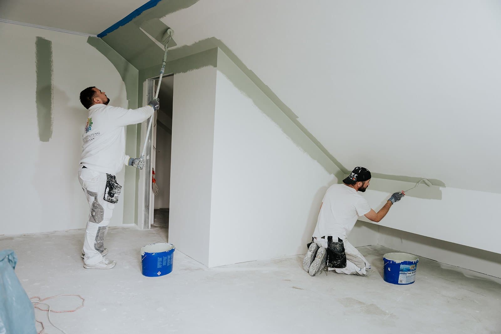 Zwei Maler arbeiten gemeinsam in einem vollständig abgedeckten Raum